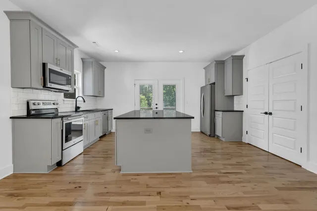 a large kitchen with stainless steel appliances granite countertop a stove a sink dishwasher a refrigerator and white cabinets with wooden floor