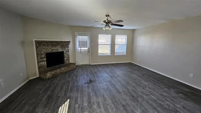 an empty room with wooden floor fireplace and windows