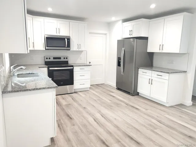 a kitchen with stainless steel appliances a stove top oven a sink a refrigerator white cabinets and wooden floor