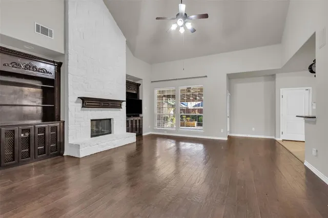 a view of a livingroom with wooden floor a ceiling fan & windows