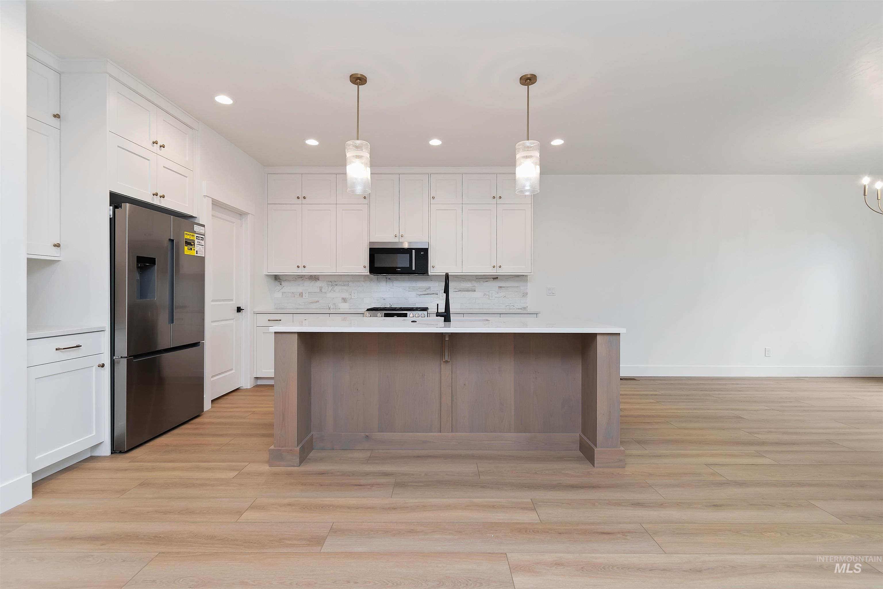 4302 Tropic Way Caldwell, ID 83607 - Photo 5 of 32 Kitchen with stainless steel appliances, a center island with sink, light wood finished floors, hanging light fixtures, and tasteful backsplash