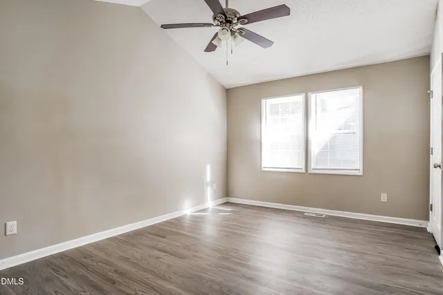 an empty room with wooden floor windows and fan