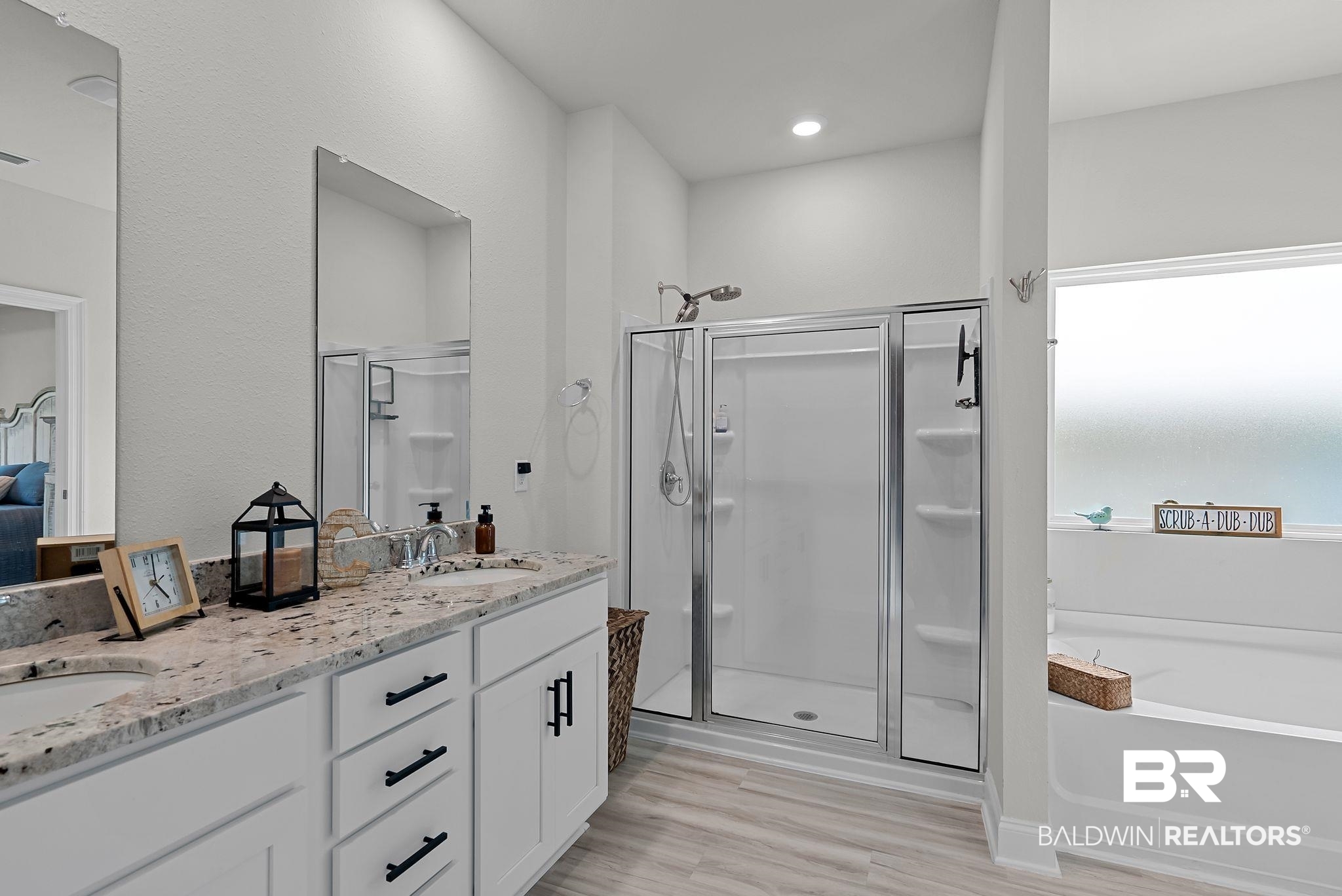 13966 Antler Hl Road Daphne, AL 36527 - Photo 18 of 44 Dual vanity with stone-finish countertop, white cabinetry with matte black hardware, glass-enclosed shower, and a built-in soaking tub under a frosted window