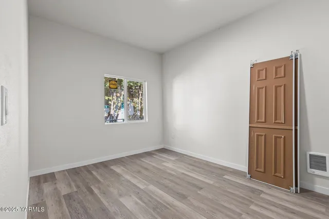 an empty room with wooden floor closet and windows