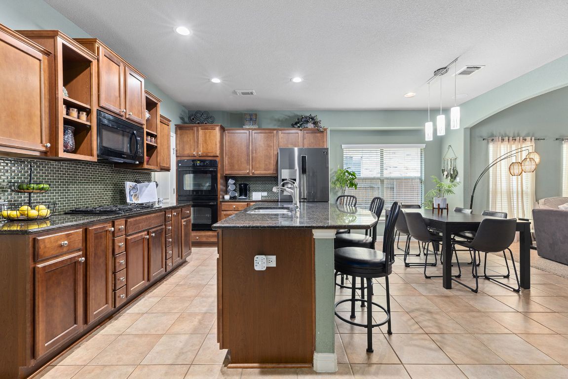 a kitchen with stainless steel appliances granite countertop a refrigerator a sink a stove a dining table and chairs