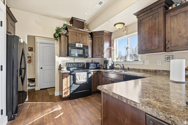1084 South 740 East Logan, UT 84321 - Photo 4 of 23 Kitchen featuring black appliances, dark wood finish cabinetry, dark wood-style floors, recessed lighting, and dark countertops