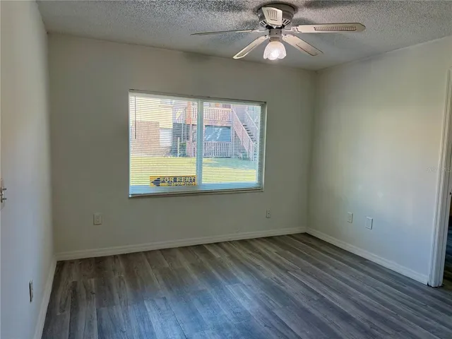 an empty room with wooden floor chandelier fan and windows