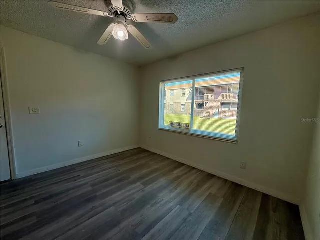 an empty room with wooden floor windows and fan