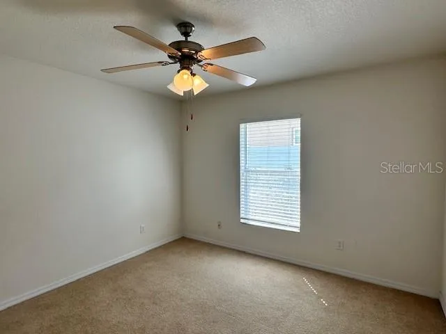 an empty room with a chandelier fan and a kitchen view
