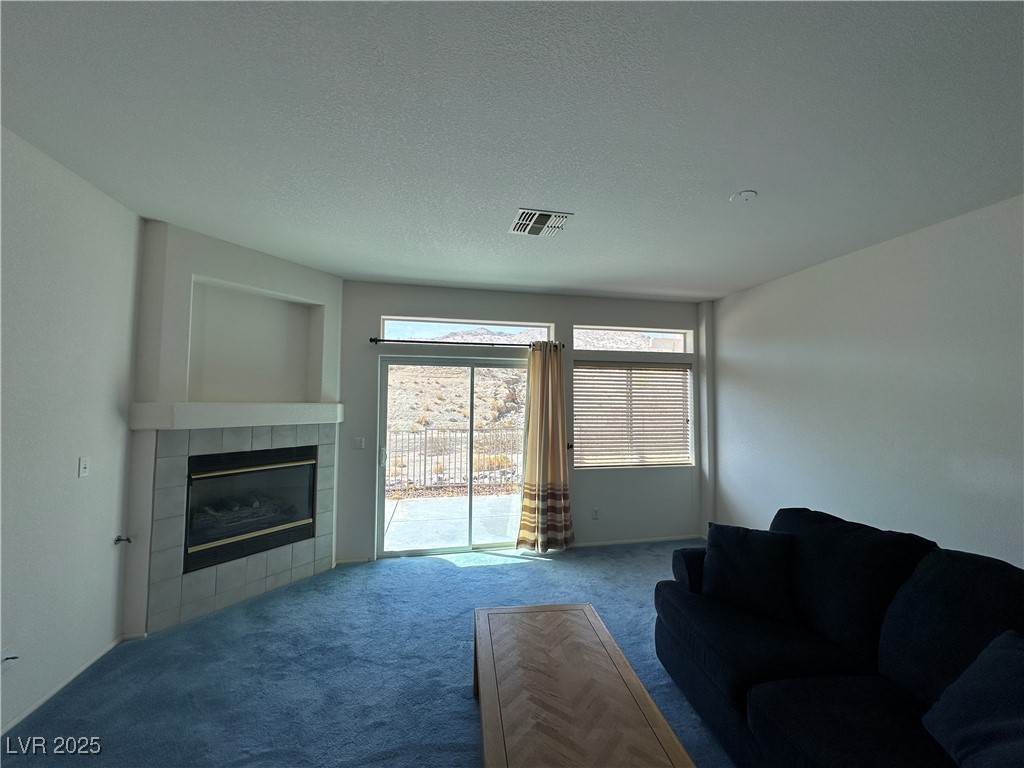 3213 Partridge Run Street Laughlin, NV 89029 - Photo 6 of 37 Carpeted living area with a tiled fireplace, visible vents, and a textured ceiling