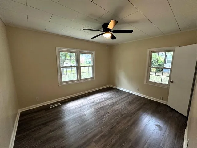 an empty room with wooden floor chandelier fan and windows