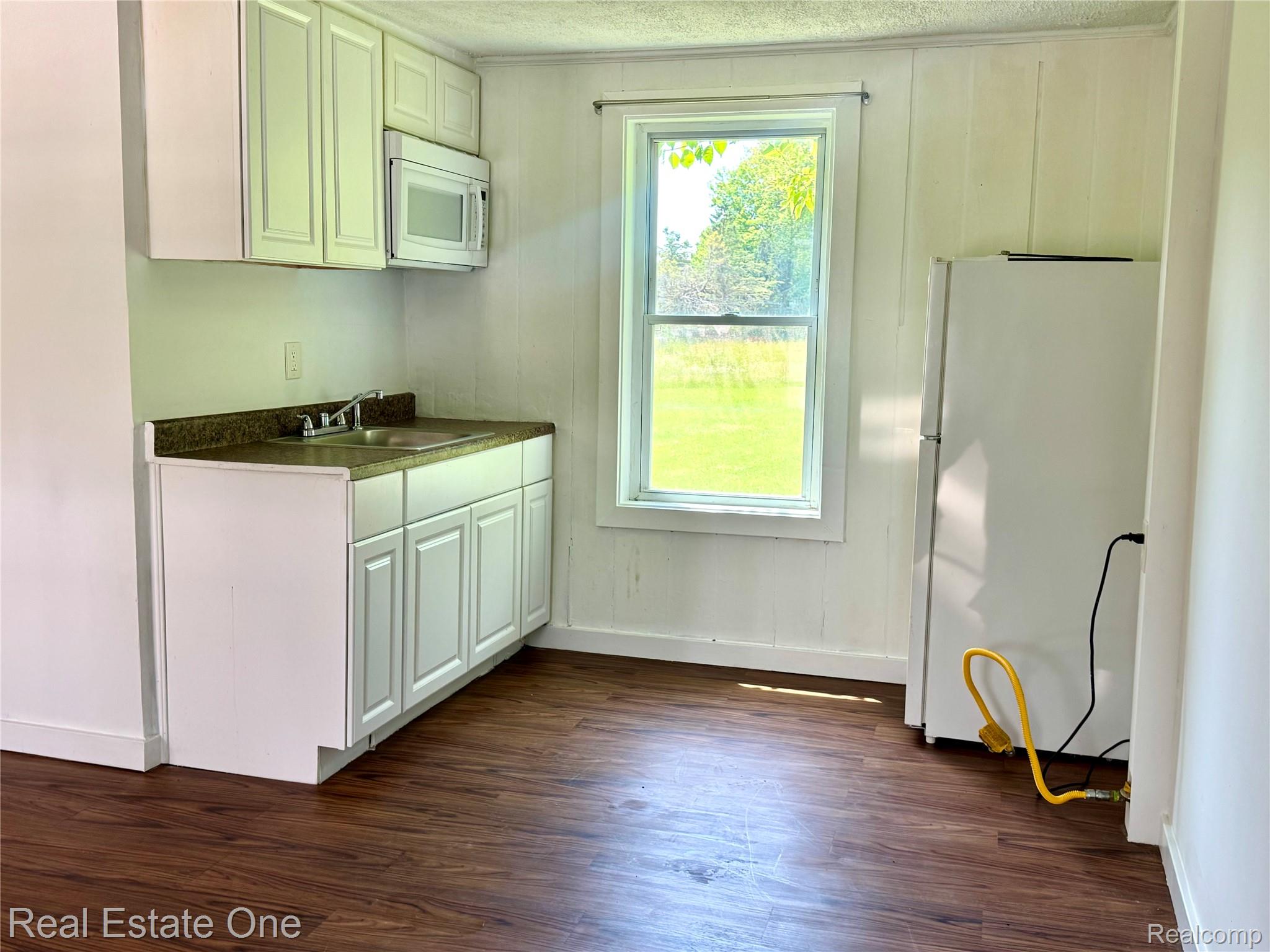 507 Lakeville Road, Unit 9 Leonard, MI 48367 - Photo 4 of 5 Compact kitchen space featuring white cabinetry, a built-in microwave, a stainless steel sink, and wood-finish flooring