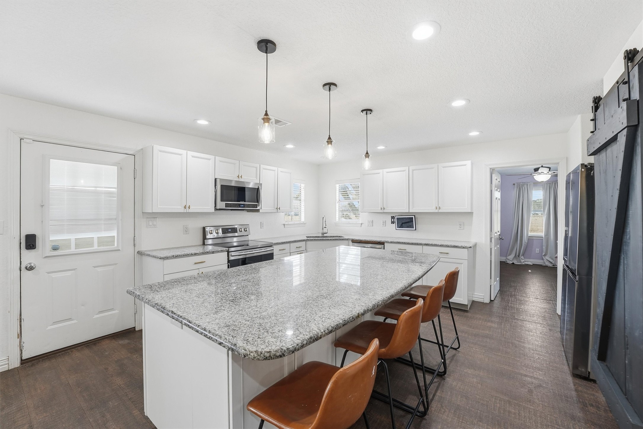 611 Reidland Road Crosby, TX 77532 - Photo 10 of 35 Spacious kitchen features modern white cabinetry, granite countertops, and stainless steel appliances. An island with seating and pendant lighting adds functionality and style, while the adjacent room offers additional living space.