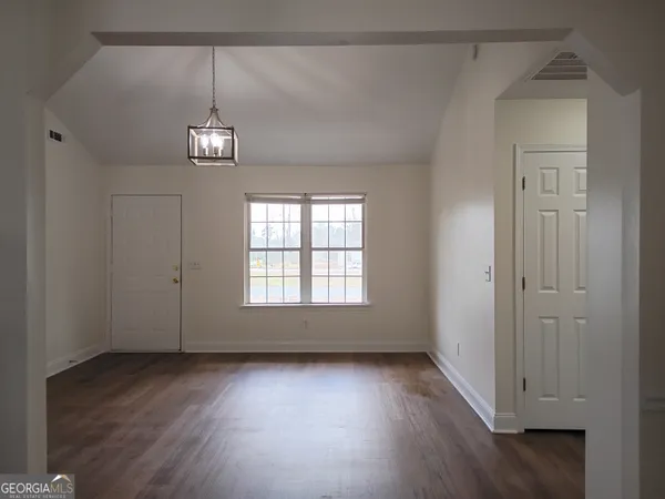 an empty room with wooden floor chandelier and windows