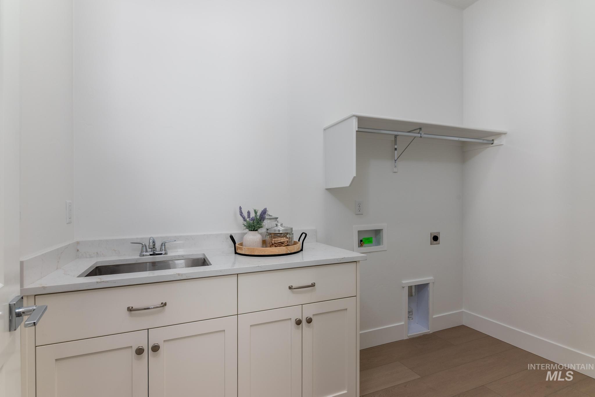 8501 South Country Wind Avenue Meridian, ID 83642 - Photo 26 of 39 Laundry room featuring white shaker-style cabinetry, a stainless steel utility sink, a light-toned wood-finish floor, a white stone-finish countertop, and a built-in shelving unit with a hanging rod