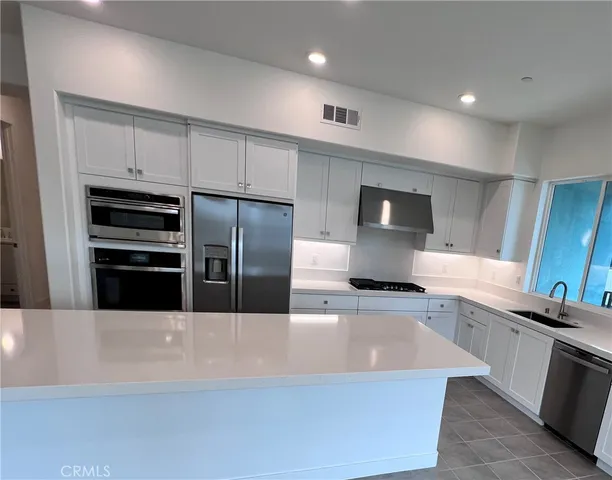 a large kitchen with stainless steel appliances a large counter top a stove a refrigerator a sink and dishwasher