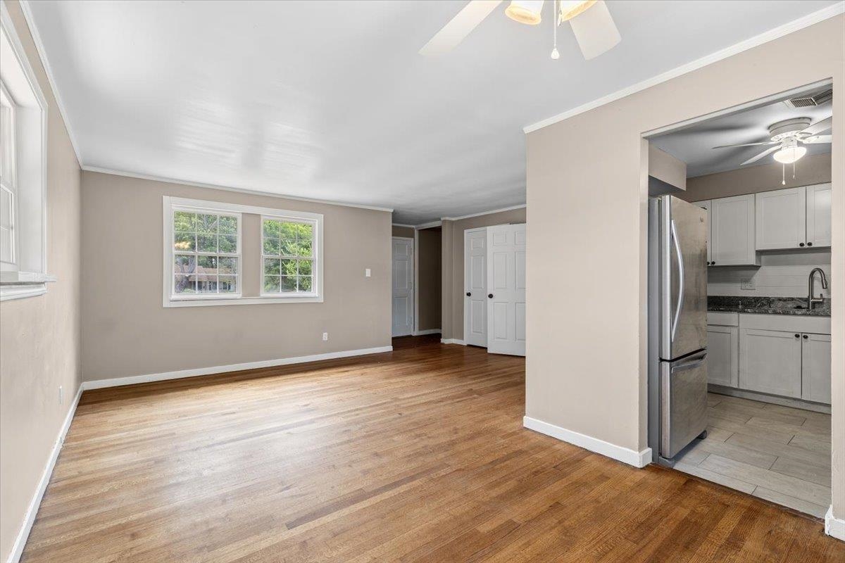 1176 South White Station Road Memphis, TN 38117 - Photo 7 of 15 Bright living area featuring wood-finish flooring, neutral paint, multiple windows, a ceiling fan, and an open doorway to the kitchen with stainless steel appliances and stone countertops