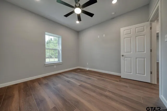 an empty room with wooden floor ceiling fan and windows