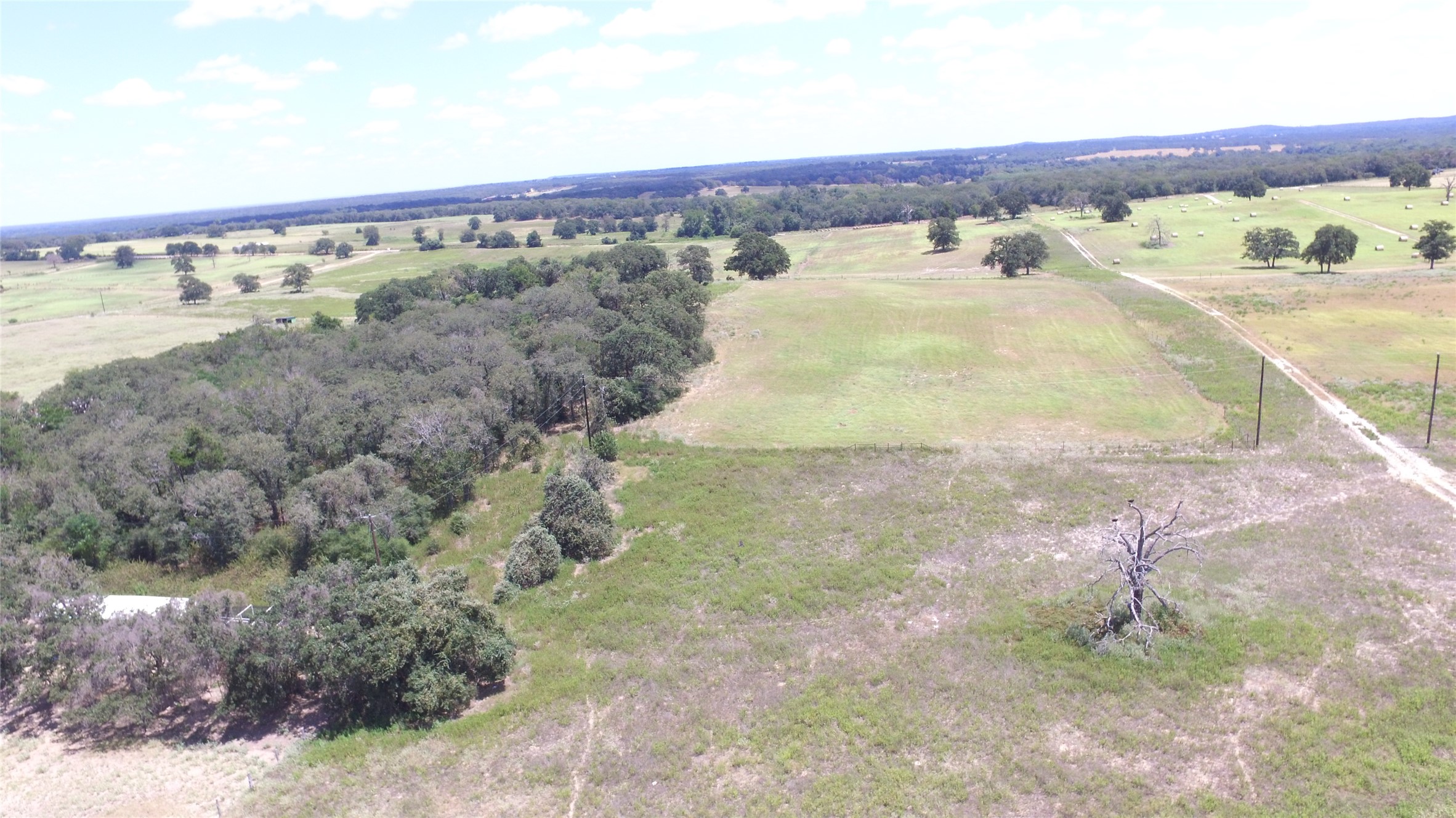 0 County Road 238 Road Cameron, TX 76520 - Photo 8 of 21 An aerial perspective reveals vast acreage of rolling green fields, woodlands, and a meandering country road.