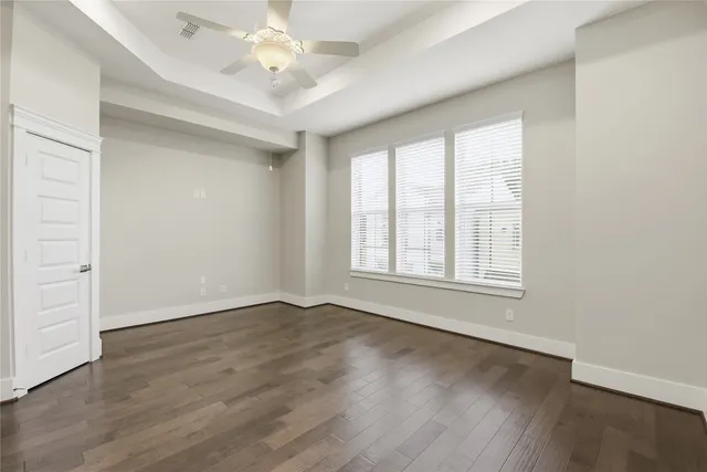 an empty room with wooden floor chandelier fan and windows