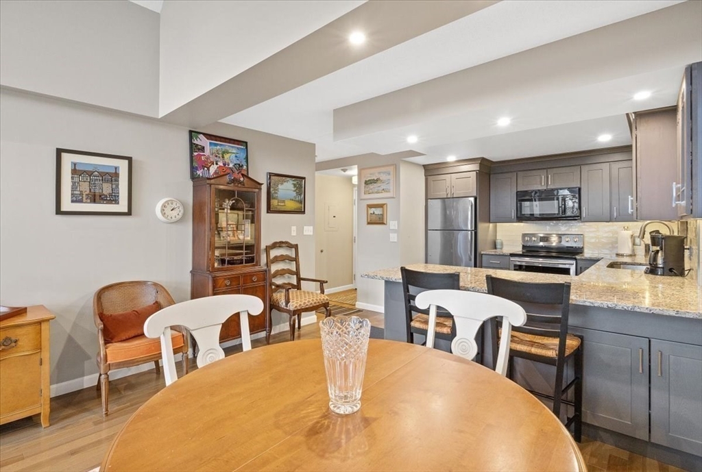 155 George Washington Boulevard, Unit 707 Hull, MA 02045 - Photo 8 of 24 a kitchen with stainless steel appliances kitchen island granite countertop a dining table chairs refrigerator and sink