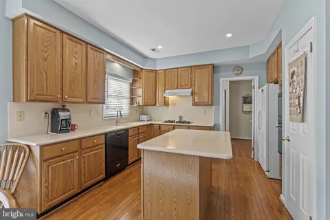 a kitchen with stainless steel appliances granite countertop a refrigerator a sink dishwasher a stove and white countertops with wooden floor
