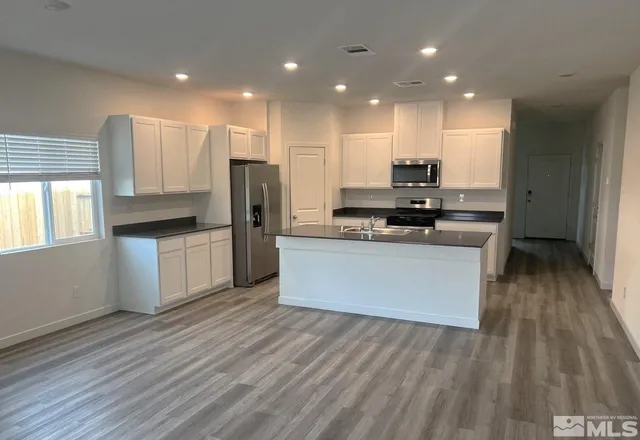 a large kitchen with stainless steel appliances granite countertop a stove a refrigerator a sink and a microwave oven on the wooden floor