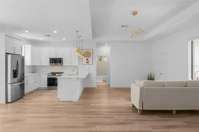 a large white kitchen with a refrigerator a stove top oven a sink dishwasher and white cabinets with wooden floor