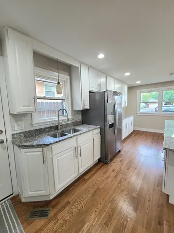 a kitchen with granite countertop a refrigerator a sink dishwasher and wooden cabinets with wooden floor