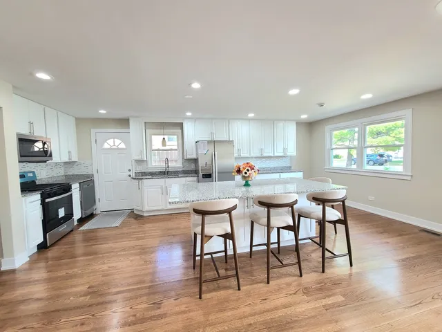 a kitchen with stainless steel appliances granite countertop a stove top oven a sink dishwasher a dining table and chairs with wooden floor