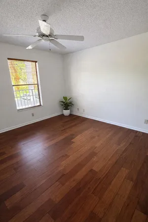 an empty room with wooden floor chandelier fan and windows