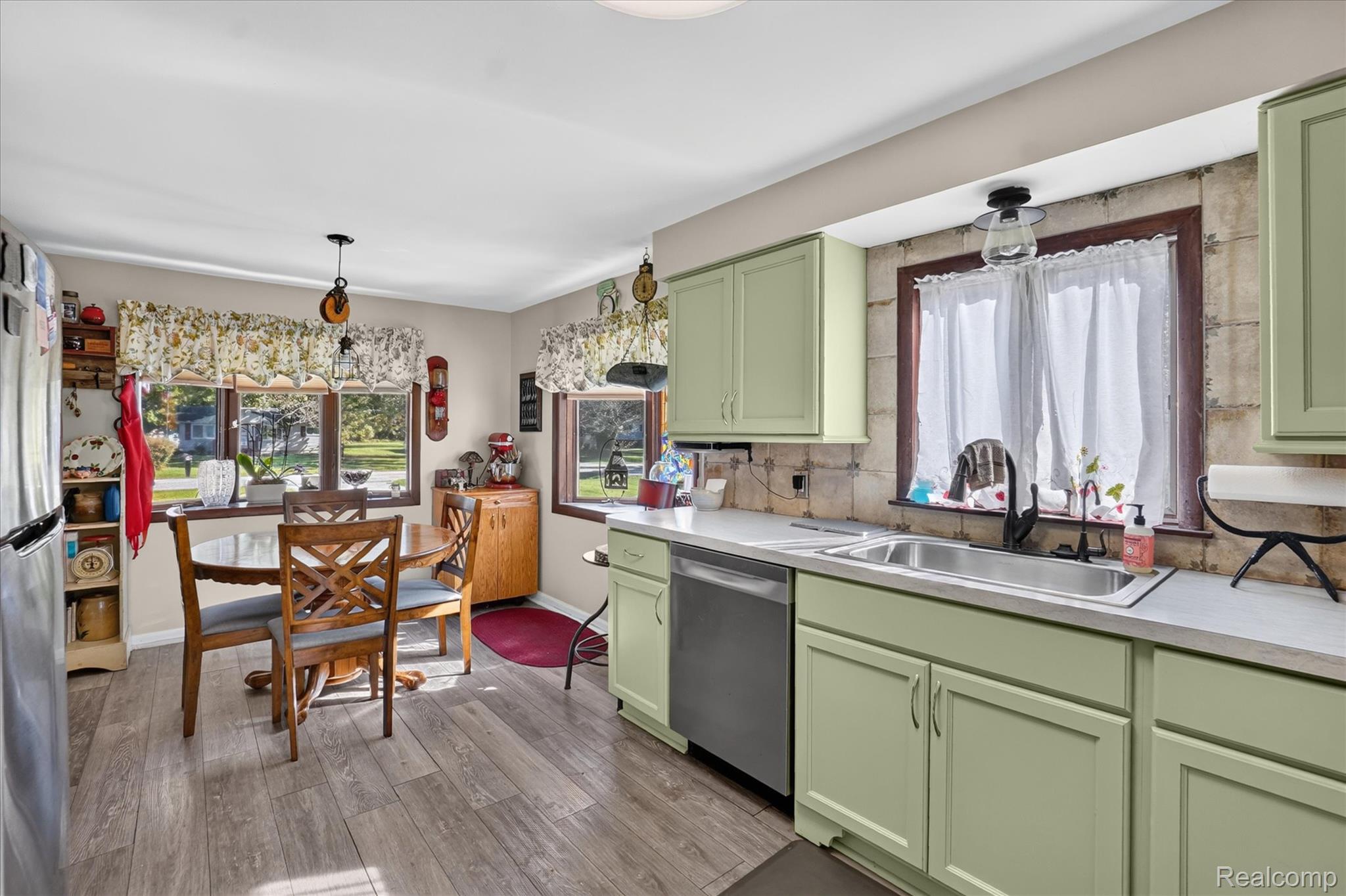 7178 Riegler Street Grand Blanc, MI 48439 - Photo 11 of 31 Kitchen featuring wood-finish flooring, light green cabinetry, a double basin stainless steel sink, a stainless steel dishwasher, and multiple windows