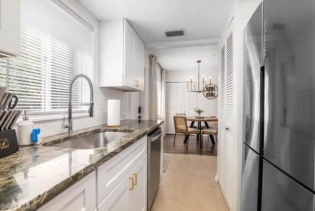 a kitchen with granite countertop a refrigerator a sink and white cabinets
