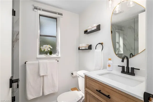 a bathroom with a granite countertop sink vanity mirror and toilet
