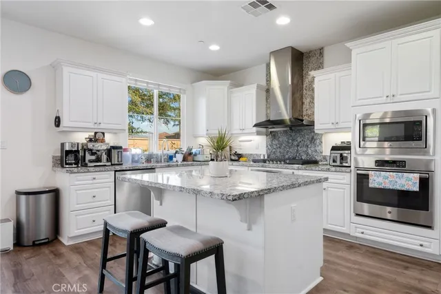 a kitchen with stainless steel appliances granite countertop a stove a sink a microwave a refrigerator and white cabinets with wooden floor