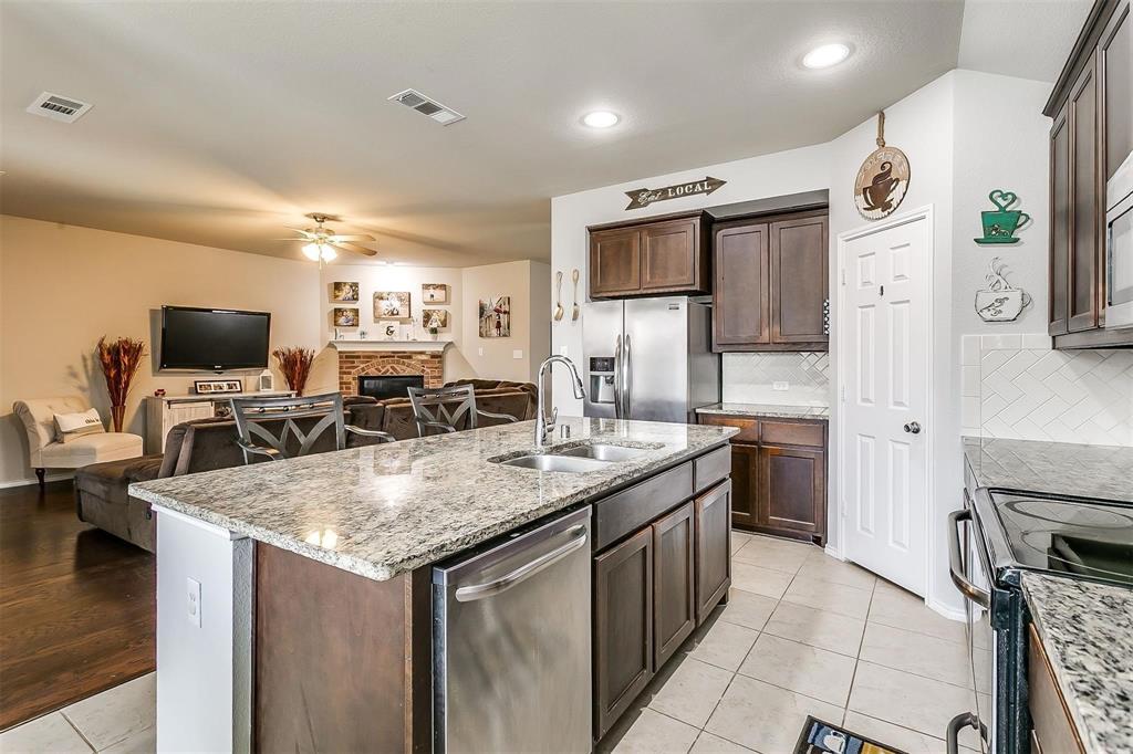 1629 Ridge Creek Lane Aubrey, TX 76227 - Photo 25 of 25 Kitchen featuring open floor plan, appliances with stainless steel finishes, a fireplace, light stone countertops, and a kitchen island with sink