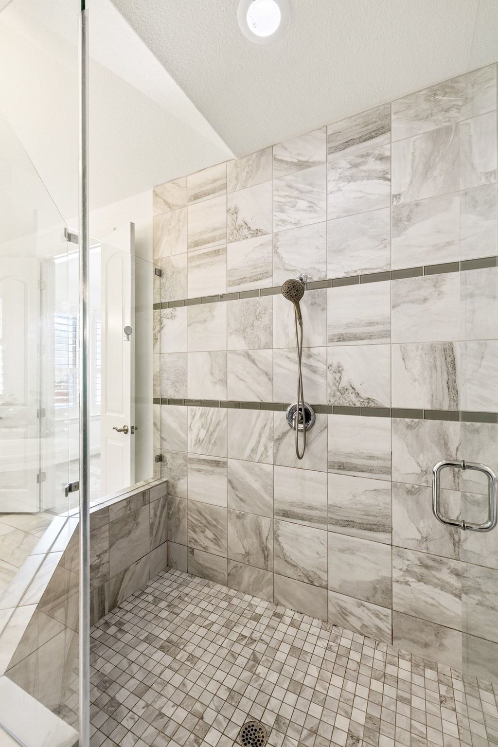 5812 Davenport Divide Road Austin, TX 78738 - Photo 24 of 40 Glass enclosed with floor-to-ceiling marble tile, detailed with a horizontal accent band and chrome fixtures. The oversized shower feels open and substantial, with a tiled floor and built-in niche for function without sacrificing design.