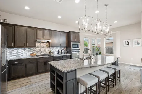 a kitchen with stainless steel appliances a stove top oven a sink dishwasher and a refrigerator with wooden floor