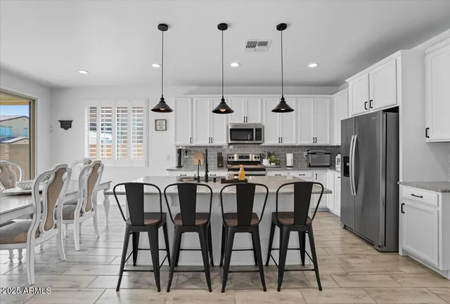 a kitchen with stainless steel appliances kitchen island granite countertop a dining table chairs and a refrigerator