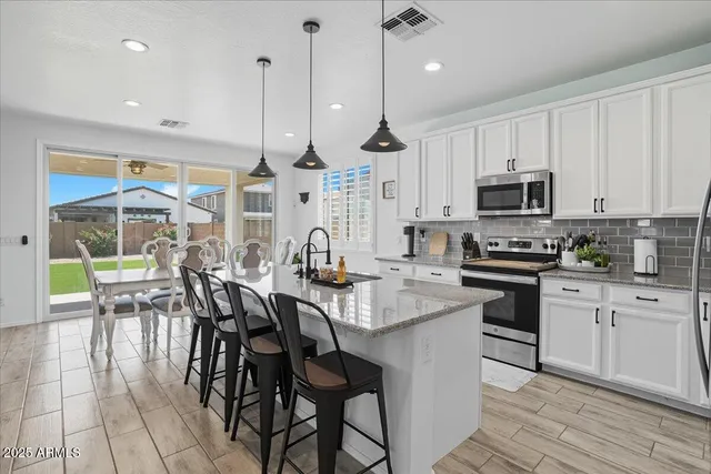 a kitchen with stainless steel appliances kitchen island granite countertop a stove a sink a dining table and chairs with white cabinets