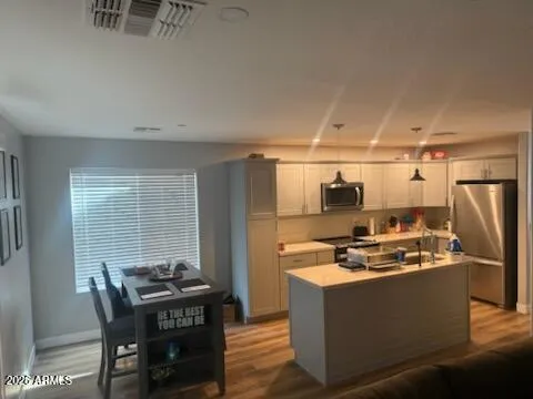 a kitchen with stainless steel appliances kitchen island granite countertop a stove a refrigerator a dining table and chairs with wooden floor