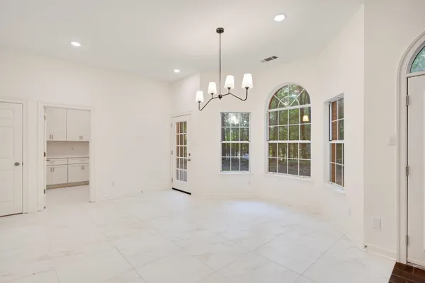 an empty room with wooden floor chandelier and windows