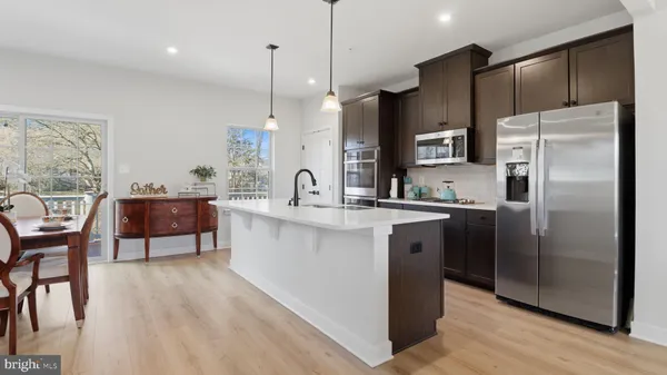 a open kitchen with stainless steel appliances granite countertop a stove a refrigerator a kitchen island a dining table and chairs with wooden floor