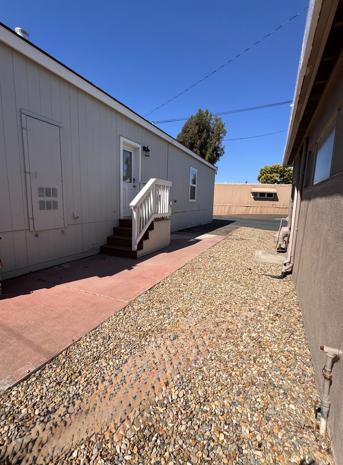 360 East Grant Line Road, Unit 16 Tracy, CA 95376 - Photo 27 of 36 Light gray siding exterior with white trim, featuring an exterior door with steps and white railing. Right side of the mobile home.