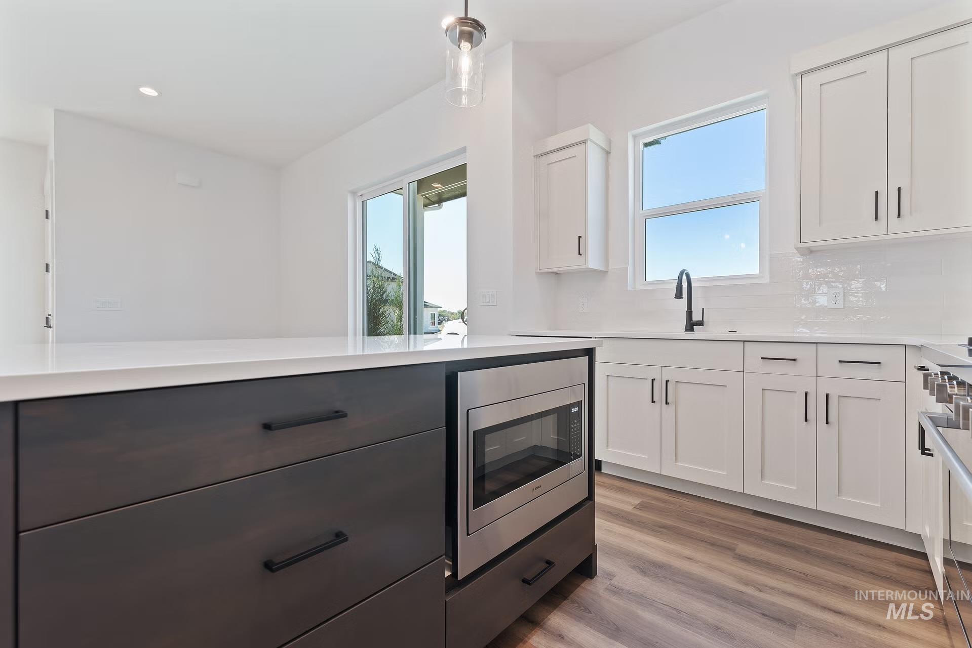 716 South Calhoun Lane Star, ID 83669 - Photo 6 of 23 Kitchen with white cabinets, stainless steel appliances, backsplash, light wood finished floors, and decorative light fixtures