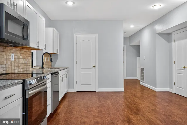 a kitchen with stainless steel appliances granite countertop a stove top oven a sink dishwasher and white cabinets with wooden floor