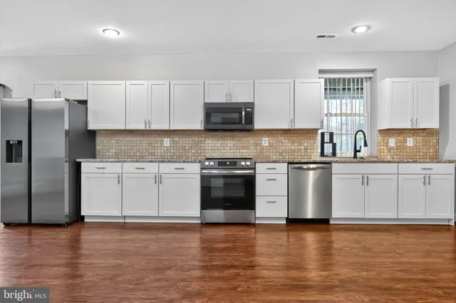 a kitchen with stainless steel appliances granite countertop a refrigerator a stove a sink and white cabinets