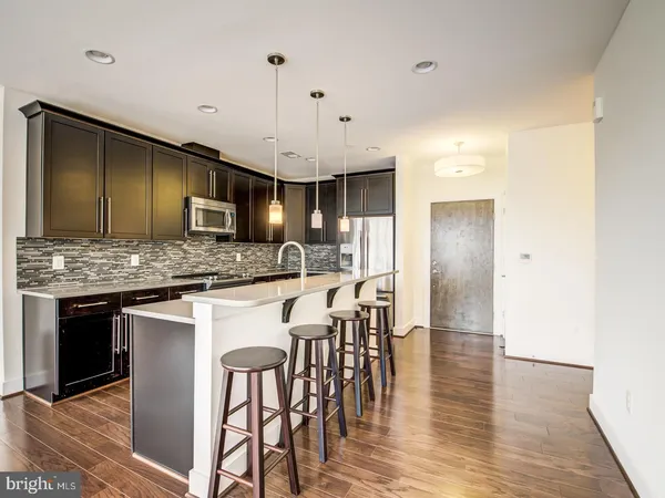a kitchen with stainless steel appliances granite countertop wooden floor a refrigerator a sink a stove and a microwave
