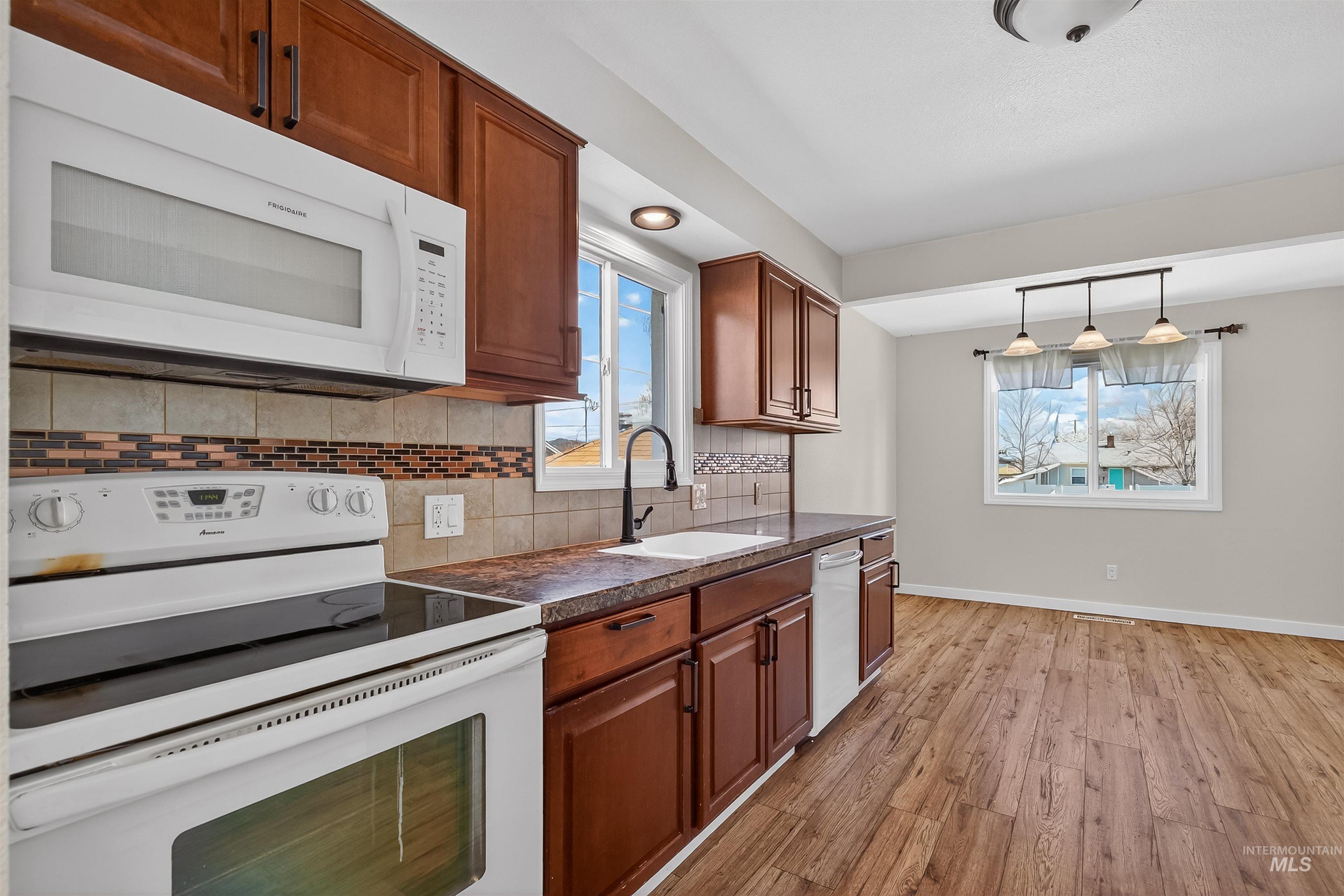 1519 17th Street Lewiston, ID 83501 - Photo 11 of 39 Kitchen with white appliances, dark countertops, light wood finished floors, wood finish cabinetry, and tasteful backsplash