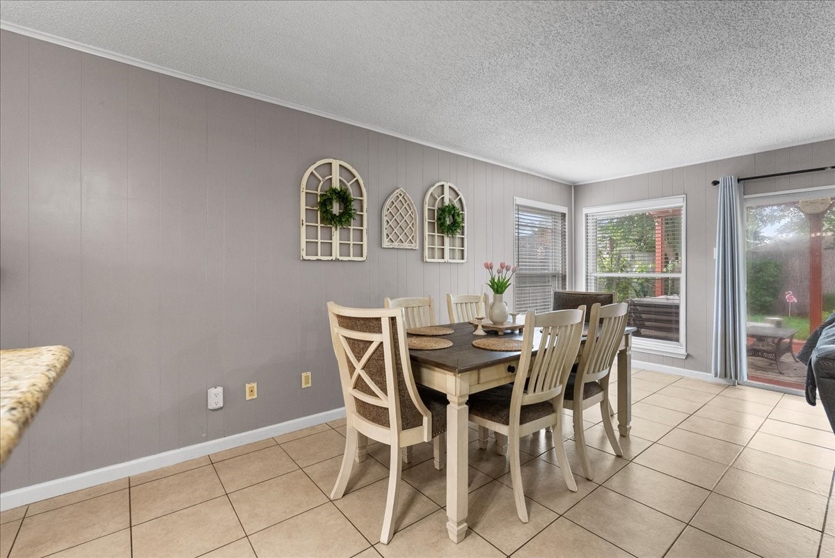 883 Silverpines Road Houston, TX 77062 - Photo 10 of 38 Bright dining area with neutral walls and tile flooring. It features a wooden table set, wall accents, and large windows offering natural light and views of the backyard. Sliding glass doors lead to an outdoor space.